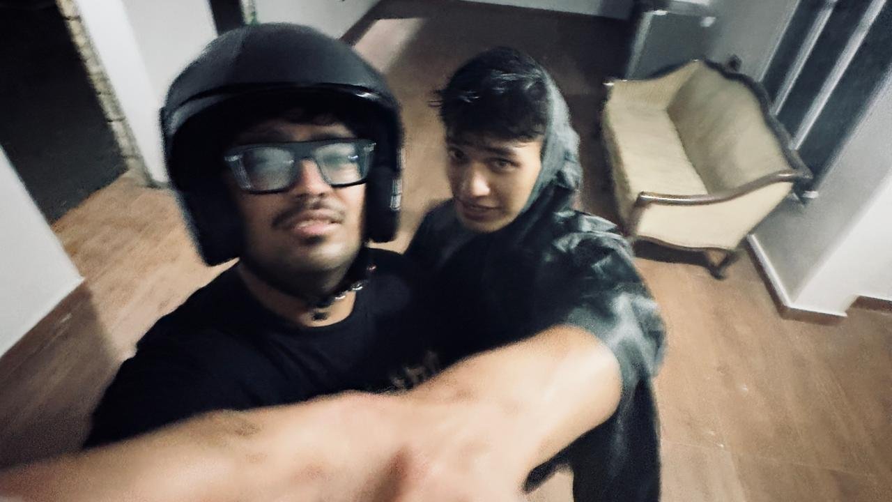 Two friends mid-selfie indoors, one wearing a motorcycle helmet